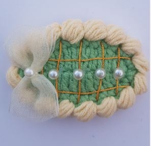 Fem perler på grønn bakgrunn med sløyfe og kremhvitt kant